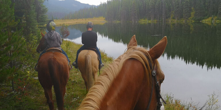 Riders on horseback beside a calm lake at dusk