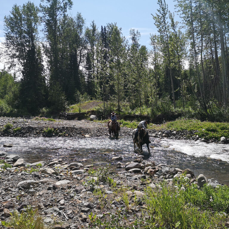 Riders crossing a wide rocky river on horseback