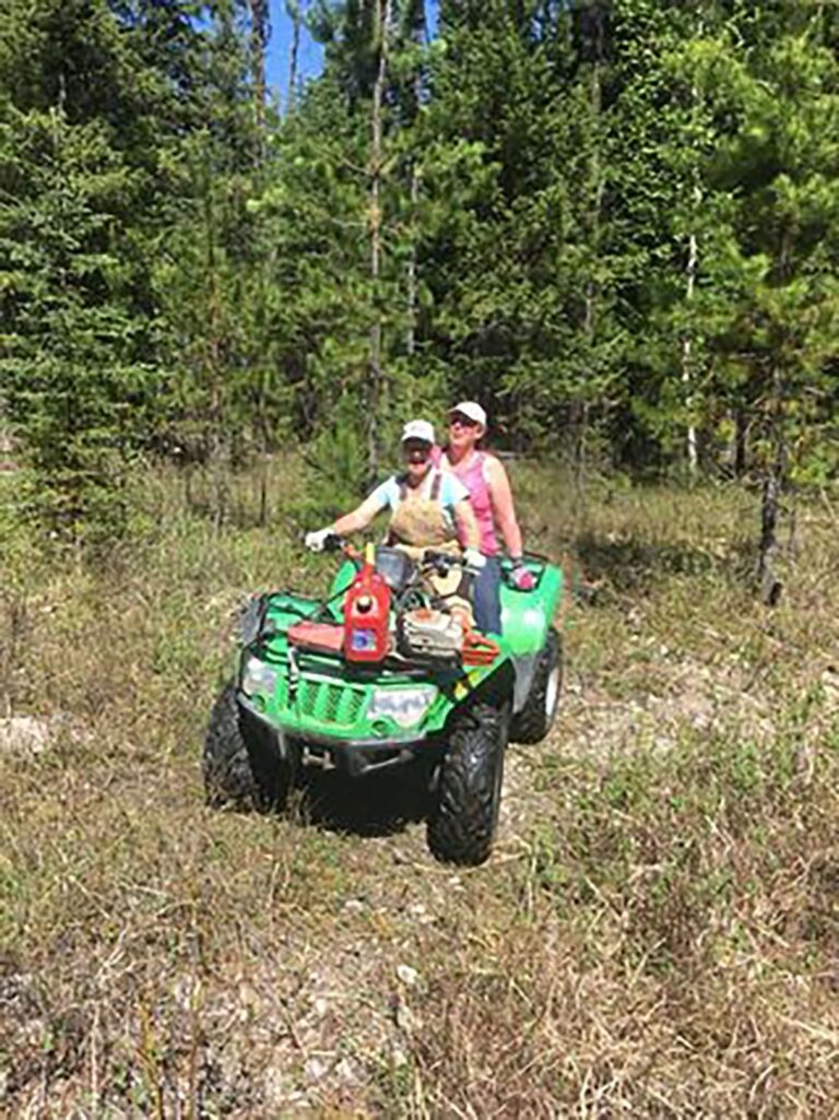 Two people on a green ATV on a forest trail