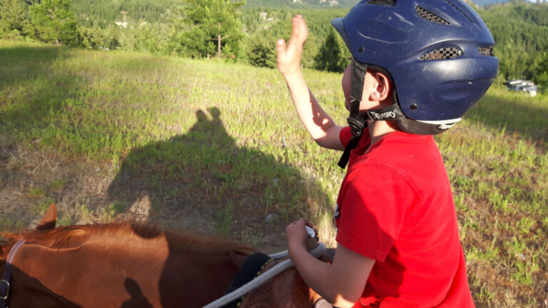 Young rider in a helmet waving from horseback