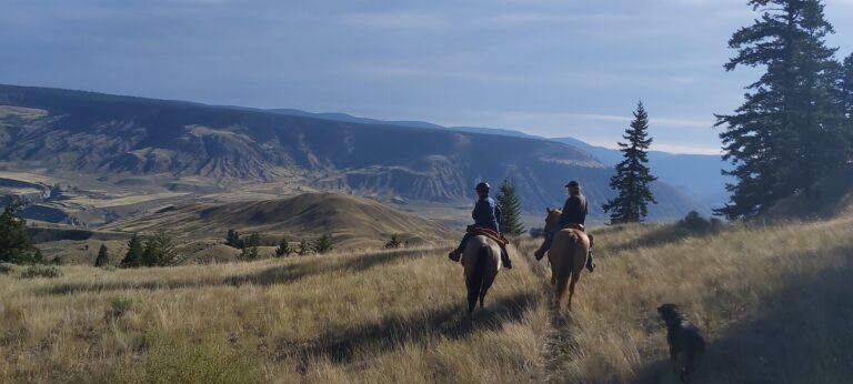 Riders on horseback on a grassy bench above a valley