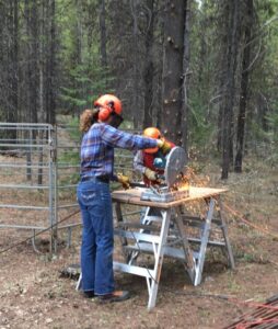 Volunteer cutting metal at a work bench at Trapping Creek camp