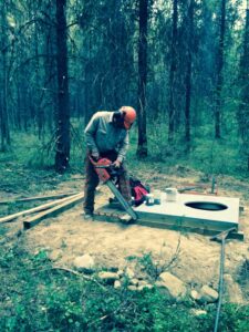 Volunteer cutting the base for a new pit toilet at Trapping Creek camp