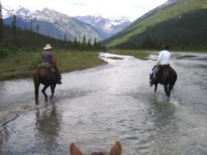 Riders crossing a glacial river below the mountains in Mount Robson Provincial Park